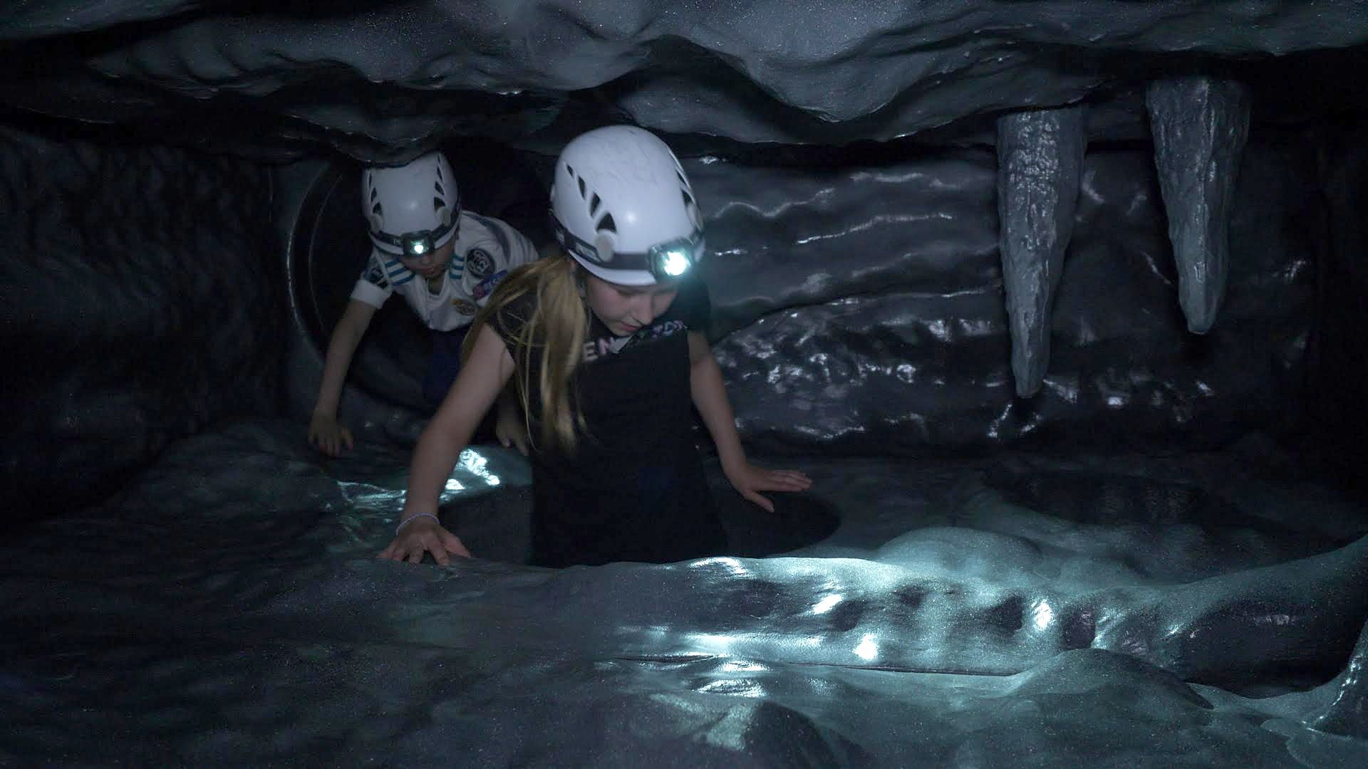 Kaksi lasta kypärissä ja otsalampuissa konttaa yhdessä luolan tunnelissa