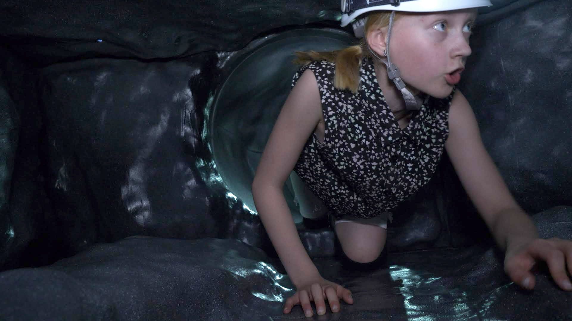 A child in a helmet and headlamp exploring a dark cave tunnel