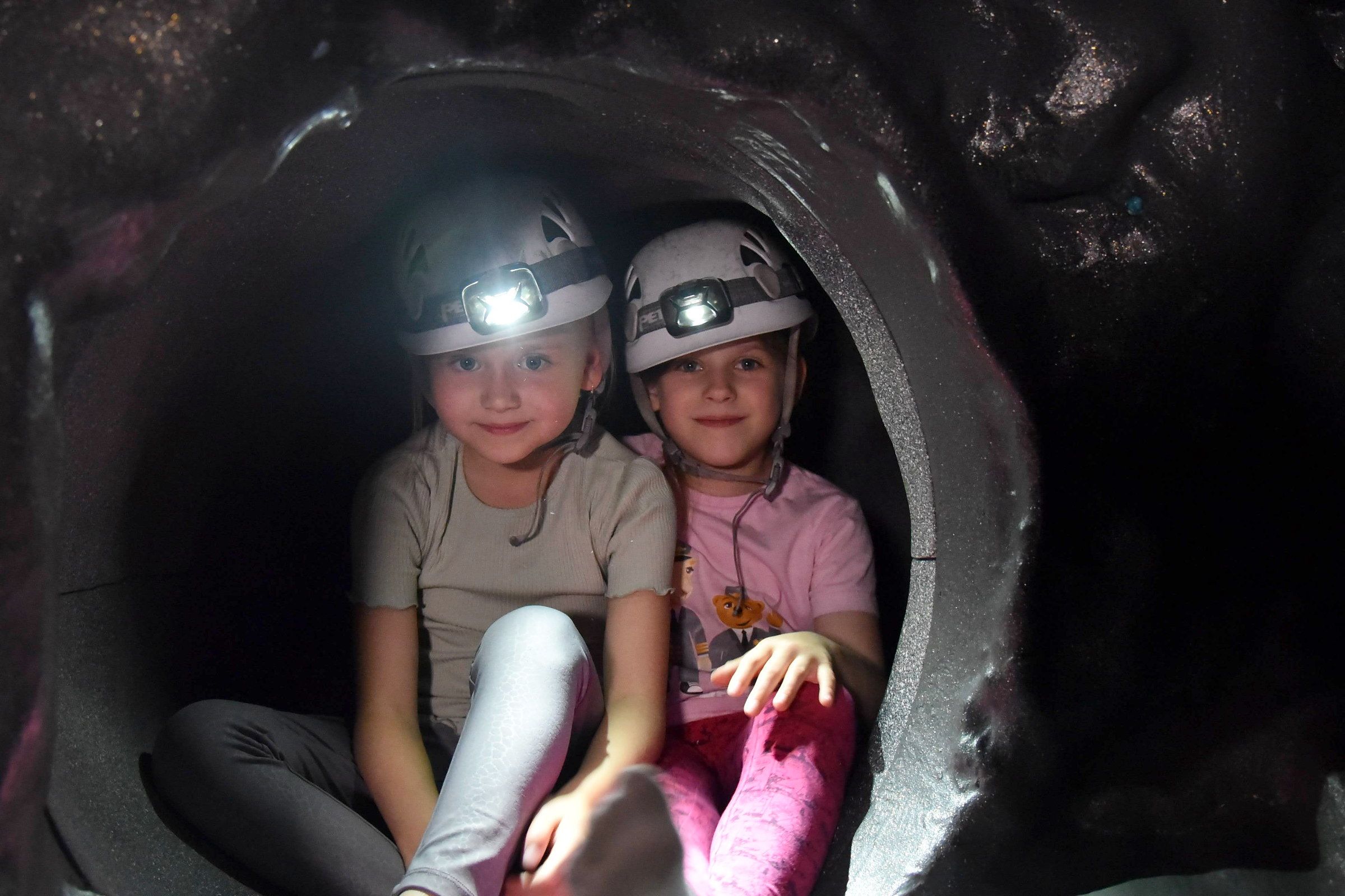 Kaksi hymyilevää lasta kypärissä ja otsalampuissa tunnelin suulla luolassa