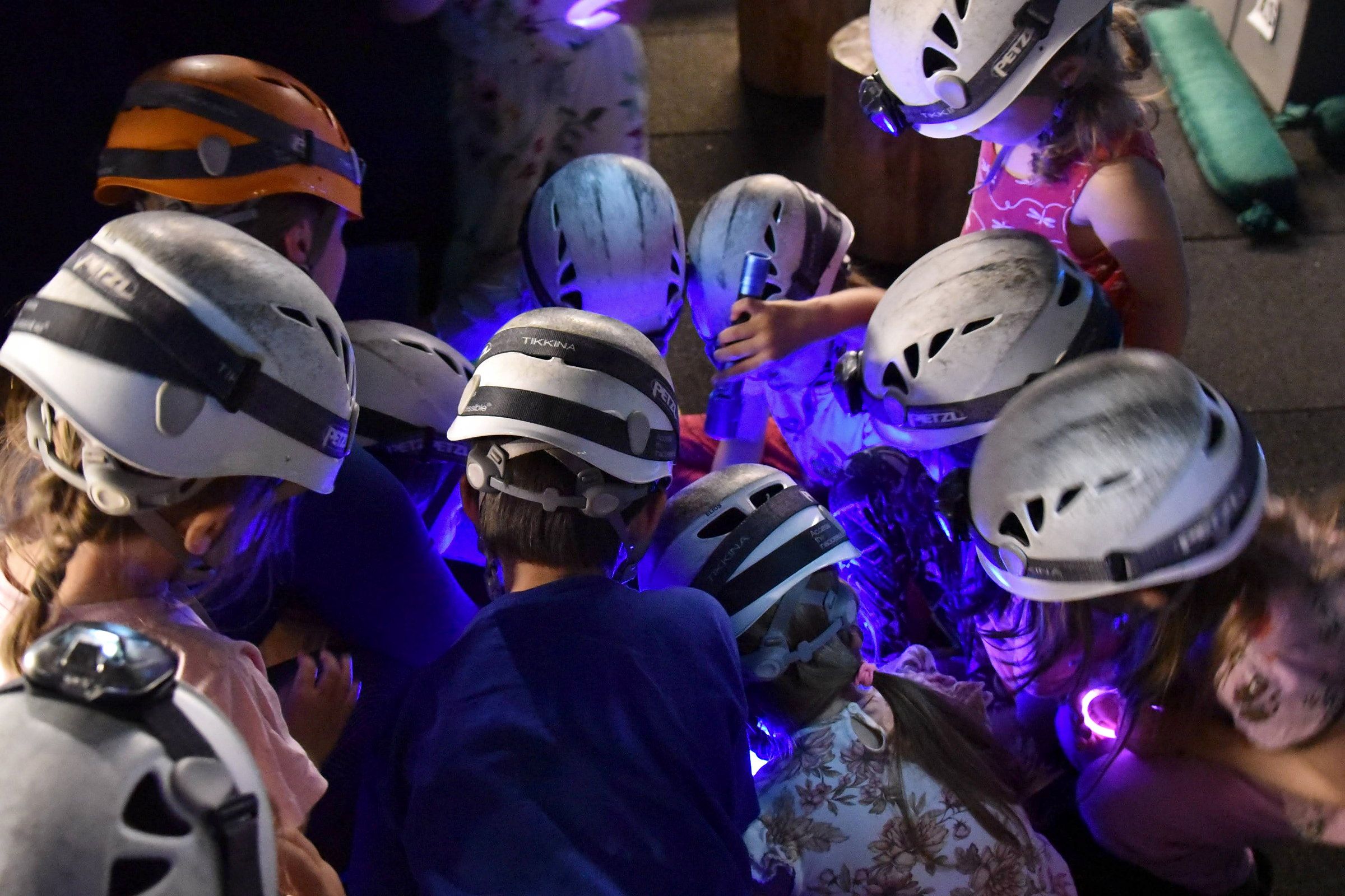 A group of children in helmets and headlamps exploring a dark cave tunnel